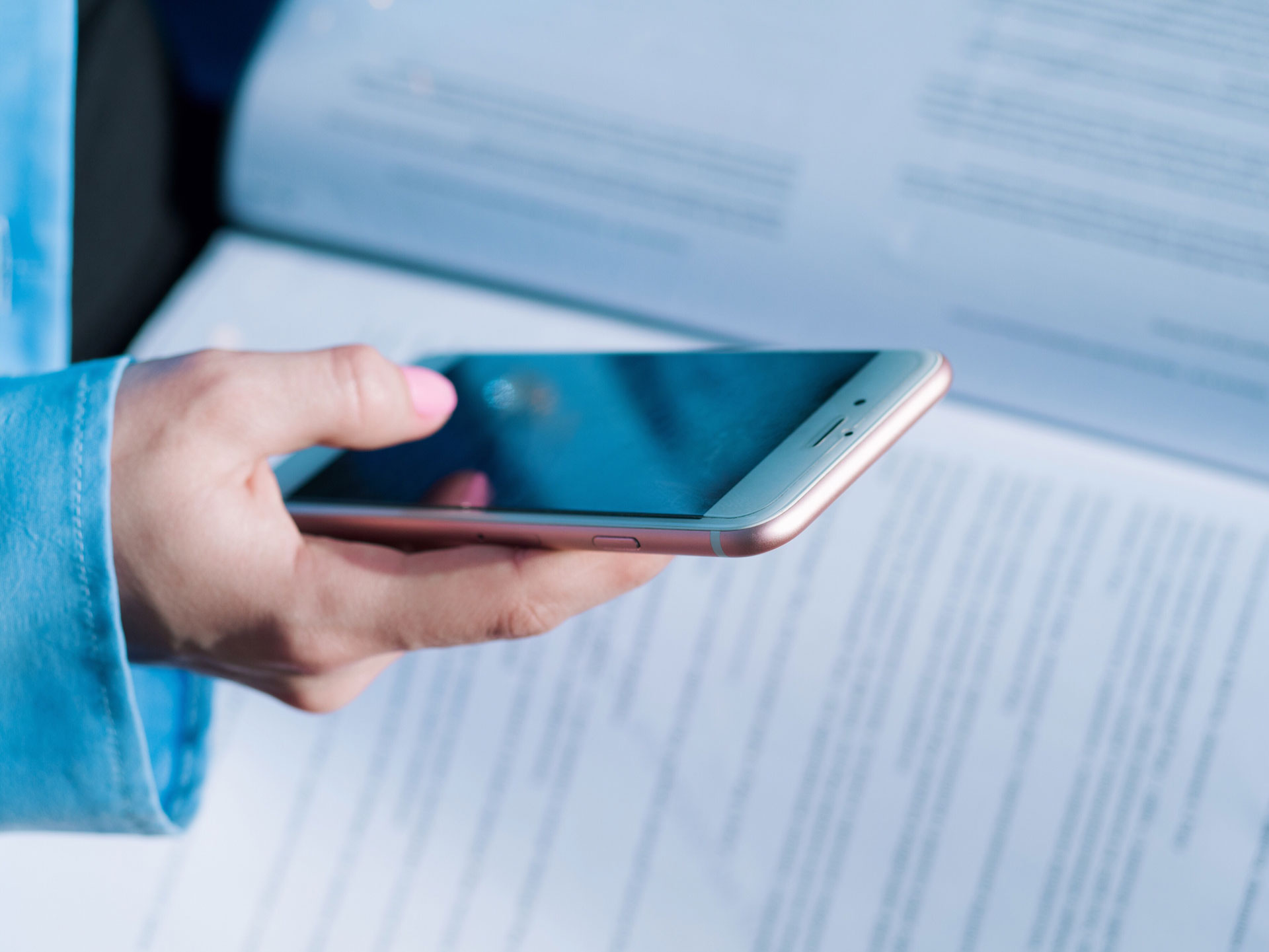 Hände einer Person, die ihr Handy benutzt. Im Hintergrund ein Buch.